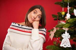 Tired woman decorating Christmas tree over red background photo