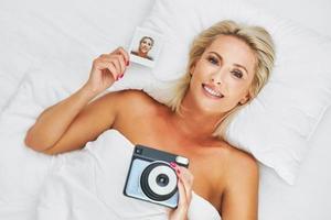 hermosa mujer adulta tomando una foto instantánea en la cama