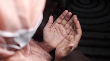 mulher de hijab e máscara facial olha para as palmas das mãos rezando video