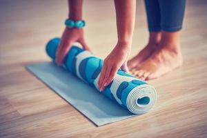 Young woman rolling yoga mat at home photo