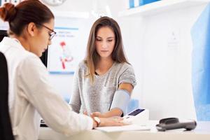 mujer adulta con prueba de presión arterial durante la visita al consultorio de una doctora foto