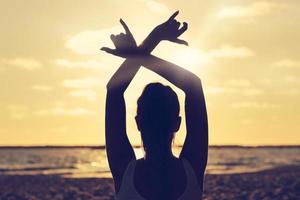 silueta, mujer joven, practicar, yoga, en la playa, en, ocaso foto