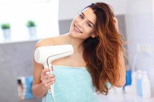 Young woman using hair dryer in bathroom in the morning photo