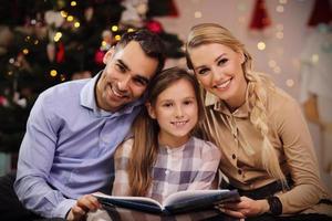 Family reading story book together under Christmas tree photo