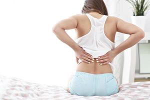 mujer joven despertando en la cama con dolor de espalda foto