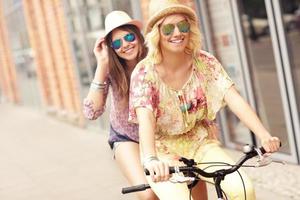 Two happy girl friends riding tandem bicycle photo