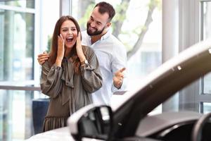 Adult man making surprise to beautiful woman in car showroom photo