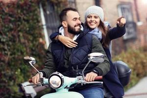 Beautiful young couple smiling while riding scooter in city in autumn photo