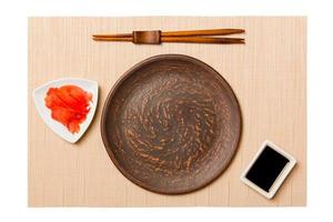 Empty round brown plate with chopsticks for sushi and soy sauce, ginger on brown sushi mat background. Top view with copy space for you design photo