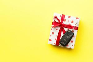 Car key on paper gift box with red ribbon bow and heart on yellow table background. Holidays present top view concept photo