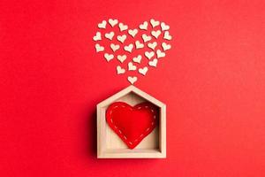 Top view of red textile heart in a wooden house decorated with small hearts on colorful background. Shape of heart. Home sweet home. Valentine's day concept photo