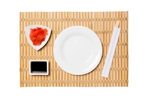 Empty oval white plate with chopsticks for sushi and soy sauce, ginger on yellow bamboo mat background. Top view with copy space for you design photo