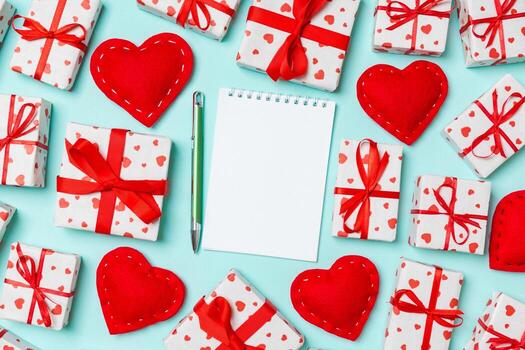 Holiday composition of notebook, gift boxes and red textile hearts on colorful background with empty space for your design. Top view of Valentine's Day concept photo