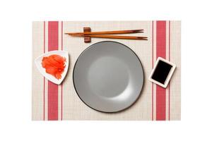 Empty round gray plate with chopsticks for sushi and soy sauce, ginger on sushi mat background. Top view with copy space for you design photo