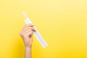 Woman's hand holding chopsticks in a pack on yellow background. Chinese food concept with empty space for your design photo