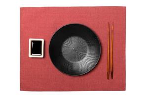 Empty round black plate with chopsticks for sushi and soy sauce on red napkin background. Top view with copy space for you design photo