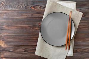 Empty grey round plate with chopsticks for sushi and soy sauce on wooden background. Top view with copy space photo