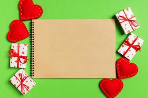 Top view of craft notebook surrounded with gift boxes and hearts on colorful background. Valentine's Day concept photo