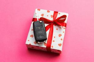 Car key on paper gift box with red ribbon bow and heart on pink table background. Holidays present top view concept photo