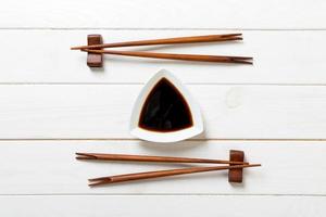 Soy sauce with chopsticks on white wooden table background photo