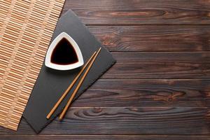 Chopsticks and soy sauce on black stone plate, wooden background with copy space photo