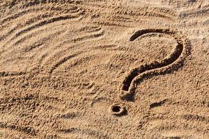 signos de interrogación escritos en la arena de la playa de cerca, con espacio de copia foto