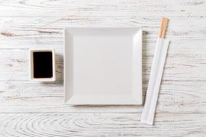 Empty white square plate with chopsticks for sushi and soy sauce on wooden background. Top view with copy space photo