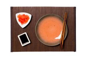 Empty round brown plate with chopsticks for sushi, ginger and soy sauce on dark bamboo mat background. Top view with copy space for you design photo