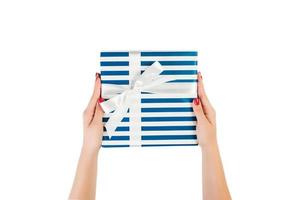 las manos de las mujeres dan Navidad envuelta u otro regalo hecho a mano en papel azul con cinta blanca. aislado sobre fondo blanco, vista superior. concepto de caja de regalo de acción de gracias foto