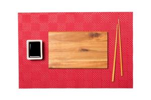 Empty rectangular brown wooden plate with chopsticks for sushi and soy sauce on red mat sushi background. Top view with copy space for you design photo