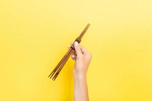Female hand holding chopsticks on yellow background. Sushi concept with empty space for your idea photo