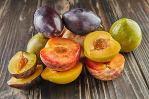 Fresh ripe plums of three colors whole and half on wooden background photo