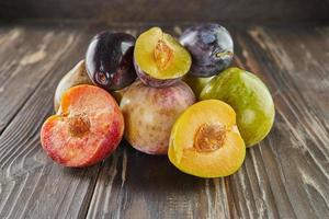 ciruelas maduras frescas de tres colores enteras y mitad sobre fondo de madera foto