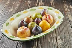 Fresh ripe plums of three colors in plate on wooden background photo