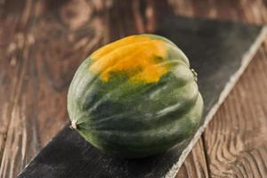 Pumpkin green-yellow on black stone on wooden background photo