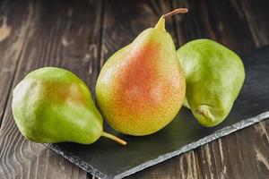 Fresh pears on black stone on wooden background photo