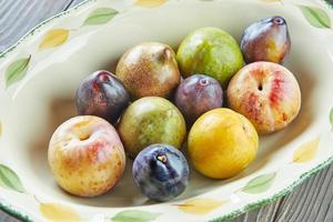 Fresh ripe plums of three colors in plate on wooden background photo