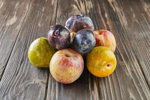 ciruelas maduras frescas de tres colores enteras y mitad sobre fondo de madera foto