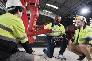 Male production engineers team discuss, test, and controls robotic arm in mechanical manufacturing factory, intelligent automatic machines in industrial business, and futuristic technology innovation. photo