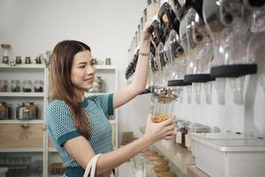 A Caucasian female customer fills cereal foods in a glass jar, lever the reusable container on refill store shelves, zero-waste and plastic-free grocery, environment-friendly, sustainable lifestyles. photo