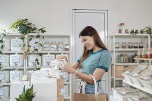 A Caucasian female customer pressed a reusable container to fill liquid products to recycle bottles at zero-waste and refill store, environment-friendly groceries, and sustainable shopping lifestyle. photo