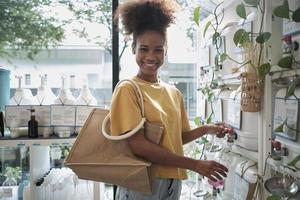 A Black female customer fills liquid soap into recycling jar from reusable containers in a zero-waste and refill store, smiles, and looks at camera, happy shopping in an environment-friendly shop. photo