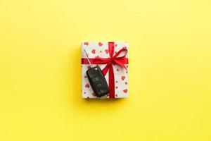 llave de coche en caja de regalo de papel con lazo de cinta roja y corazón sobre fondo de mesa amarillo. concepto de vista superior actual de vacaciones foto