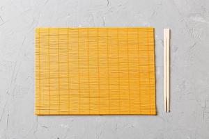 two sushi chopsticks with empty bamboo mat or wood plate on stone Background Top view with copy stace photo