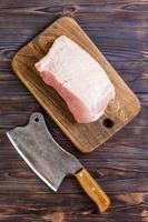 Raw cut of pork shoulder on board with knife or Kitchen ax. cleaver with fresh raw meat on black wooden background photo