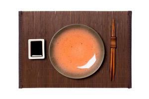 Empty round brown plate with chopsticks for sushi and soy sauce on dark bamboo mat background. Top view with copy space for you design photo