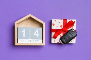Top view of car key on a gift box with red hearts and festive calendar on colorful background. The fourteenth of february. Present for Valentine's Day concept photo