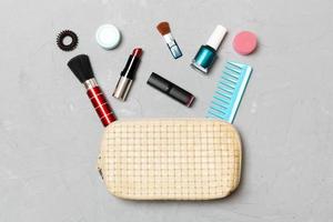 vista superior del conjunto de productos de maquillaje y cuidado de la piel que se derraman de la bolsa de cosméticos sobre fondo de cemento. concepto de belleza foto