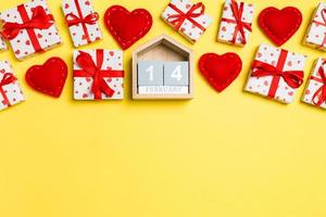 Holiday composition of gift boxes, wooden calendar and red textile hearts on colorful background with empty space for your design. The fourteenth of February. Top view of Valentine's Day concept photo