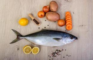 pescado fresco con limón, perejil y especias en tabla de cortar de madera aislada foto